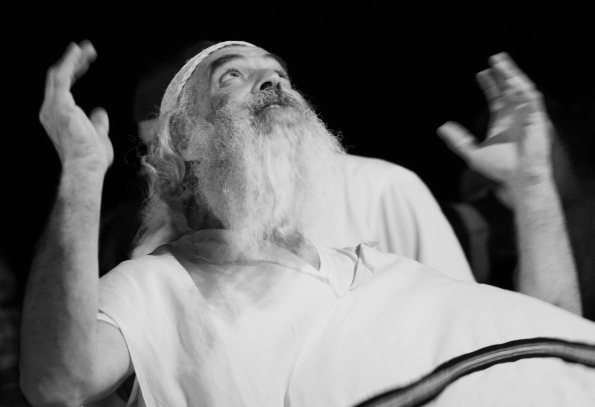 A bearded man in a white robe raises both hands and looks upward in prayer at night, Arava Desert
