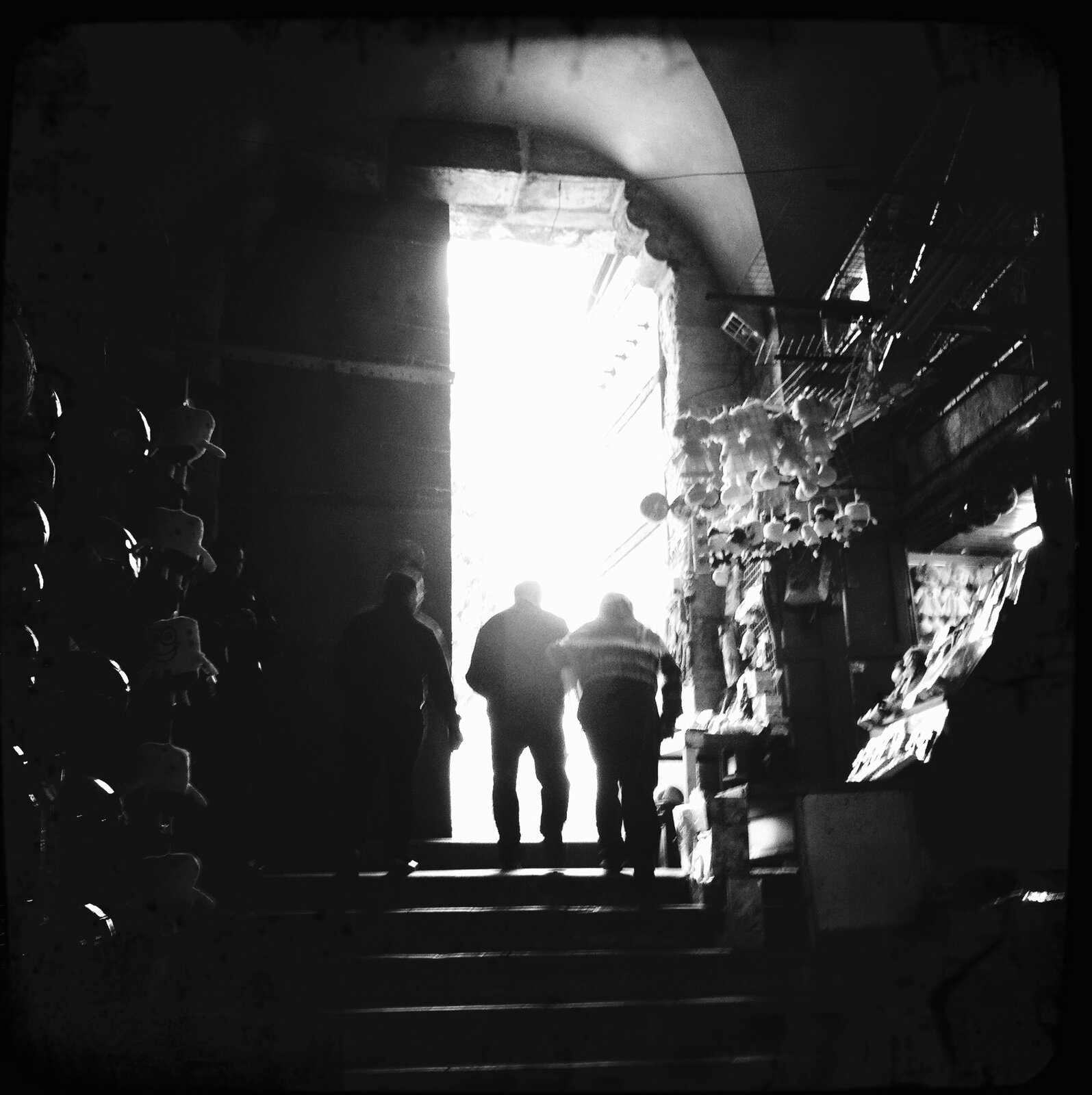Three silhouetted figures walking into bright light through a stone archway, Old City, Jerusalem