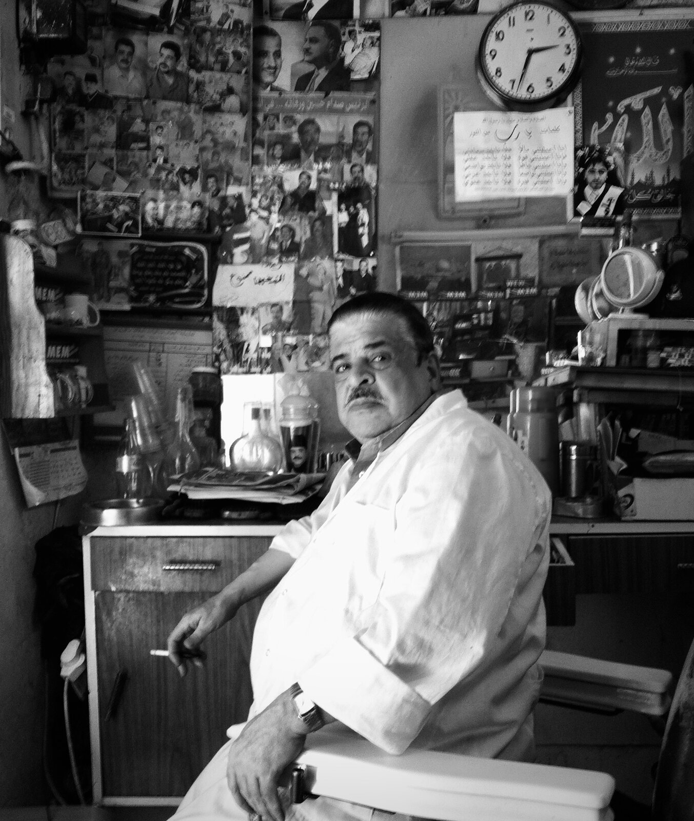 Shopkeeper in a white coat beneath a wall covered in photographs, Old City, Jerusalem
