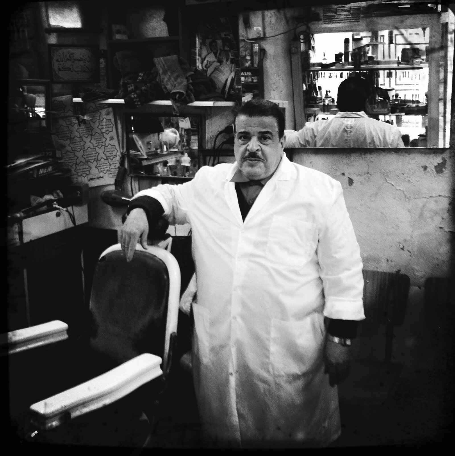 Barber standing beside his chair in a small Old City barbershop, Jerusalem