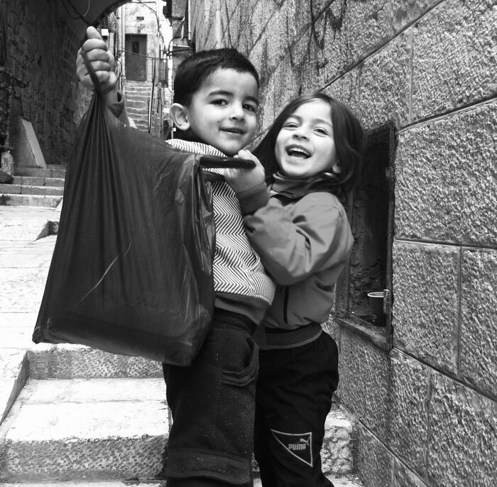 A boy holding up a shopping bag beside a laughing girl, Old City alley, Jerusalem