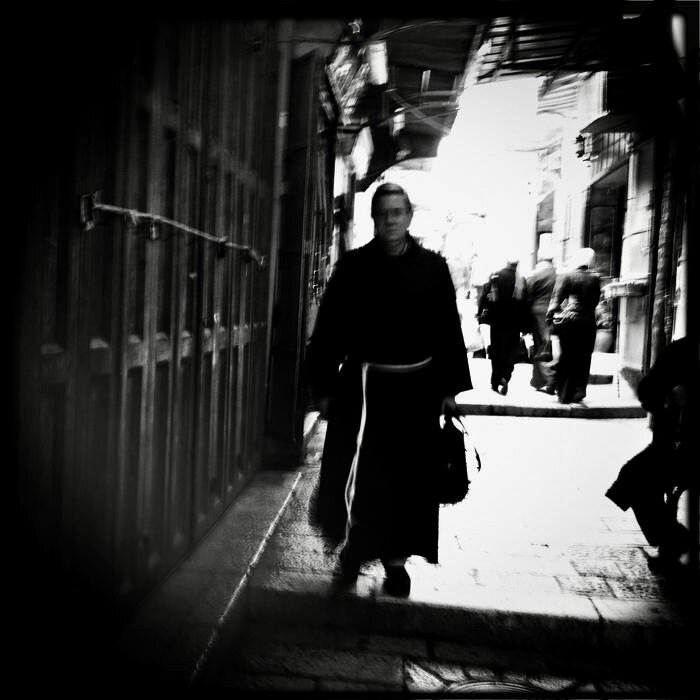 A monk in dark robes walking through a sunlit alley, Old City, Jerusalem