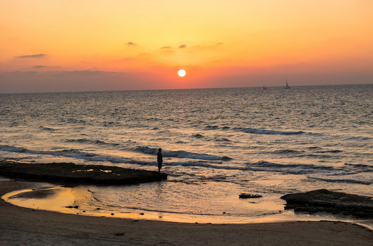 Man standing at the water's edge at sunset, Tel Aviv
