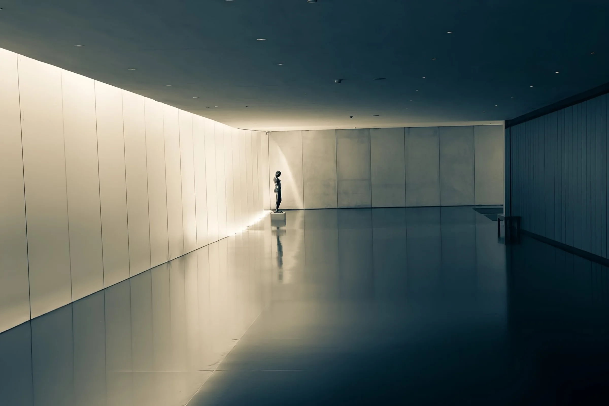 A small bronze figure stands alone at the end of a long, softly lit corridor, Israel Museum, Jerusalem