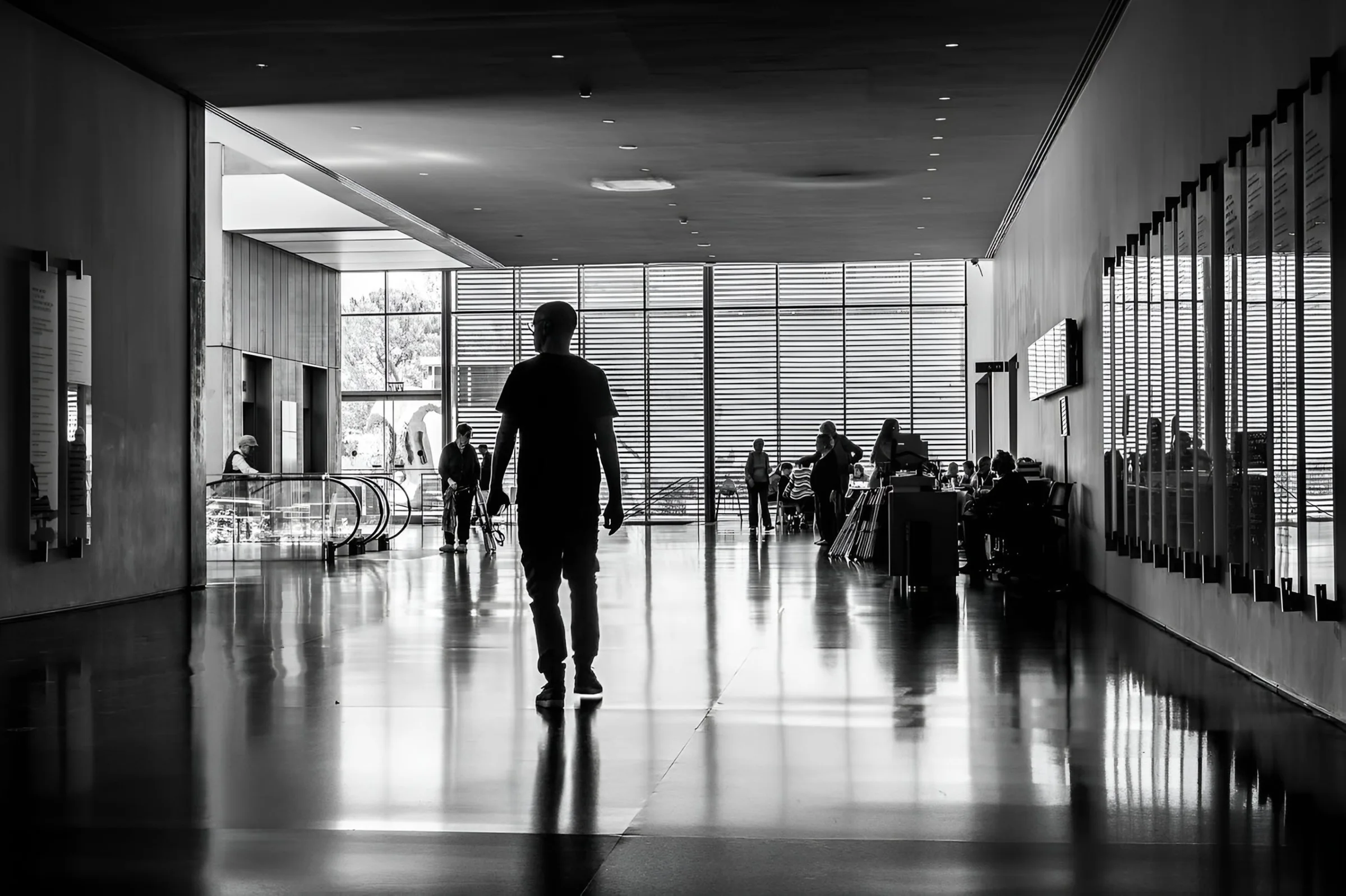 Silhouette of a man walking through a hall of the Israel Museum, Jerusalem, toward a louvered glass wall, reflections on the polished floor