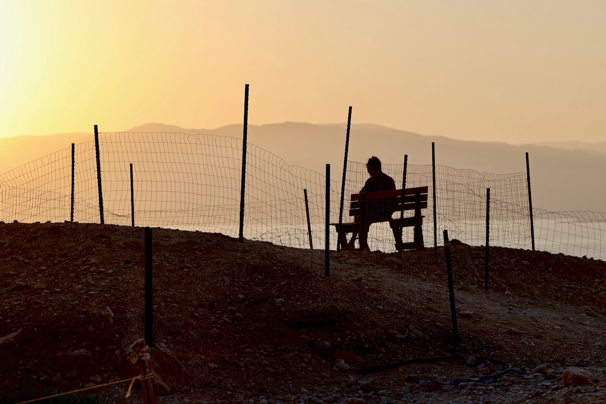 Man on a bench surrounded by wire fence at Dead Sea sunrise